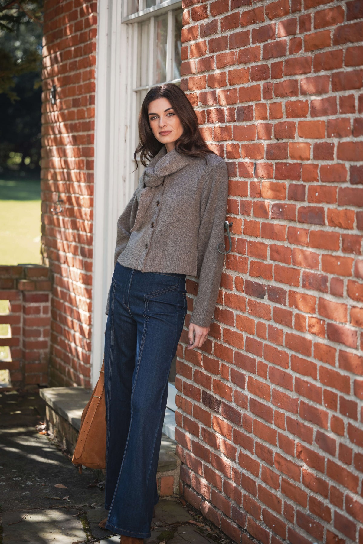 Gray button-front cardigan with attached scarf collar worn with dark denim jeans and brown shoulder bag.
