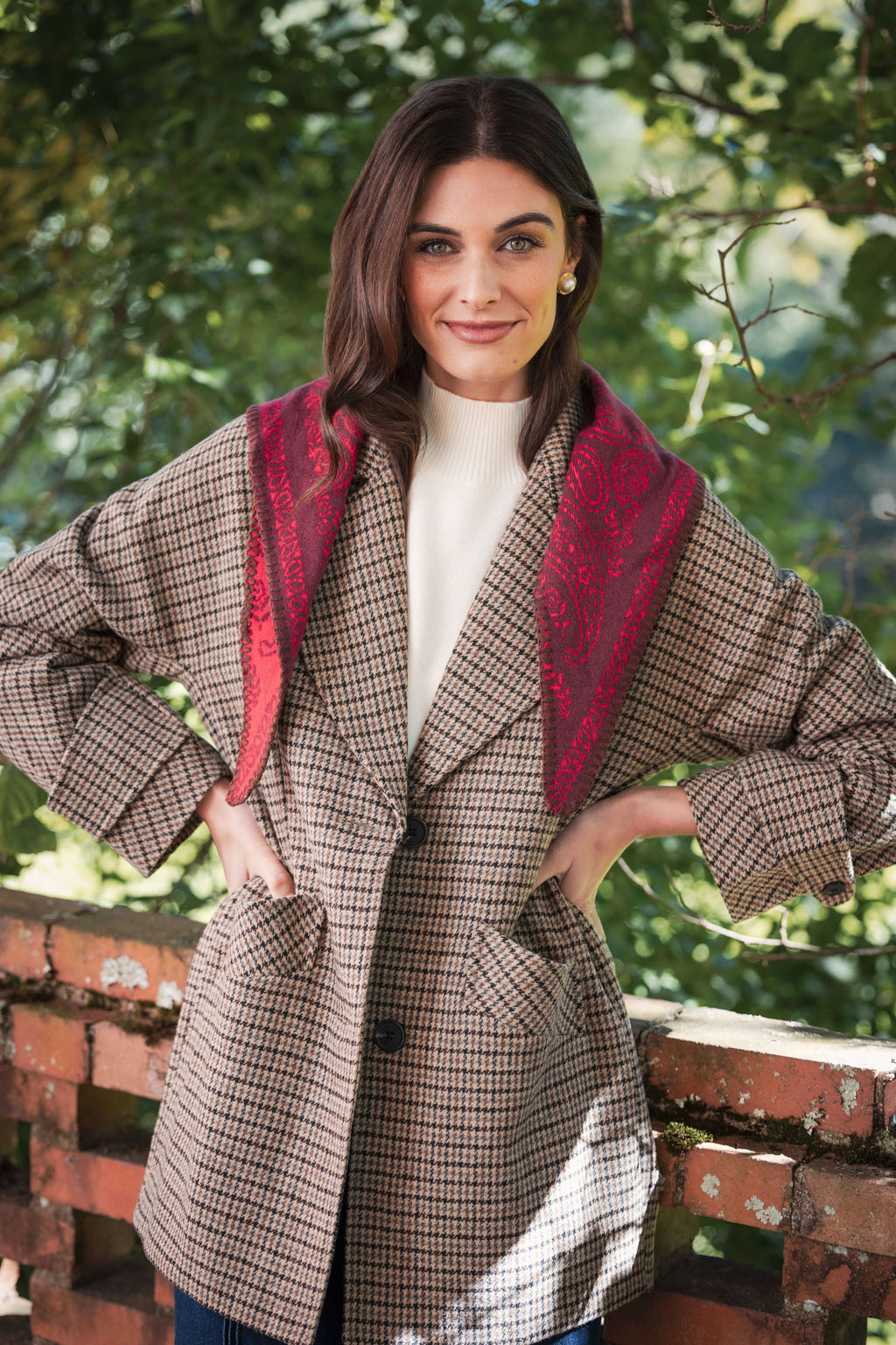 Woman wearing a beige and black houndstooth pea jacket with a red patterned collar over a cream turtleneck.