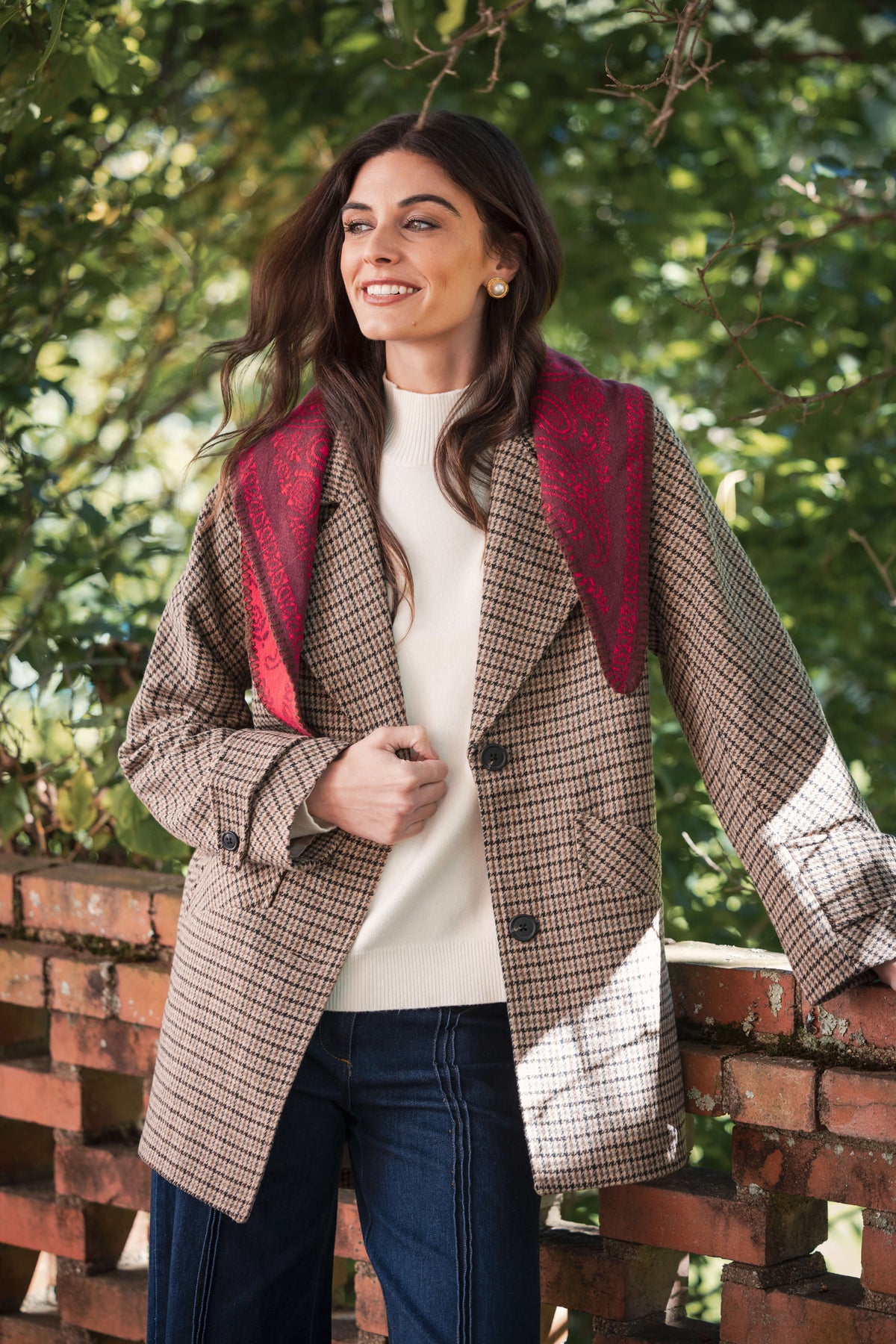 Woman wearing cream mockneck sweater with houndstooth blazer and red scarf over dark jeans.