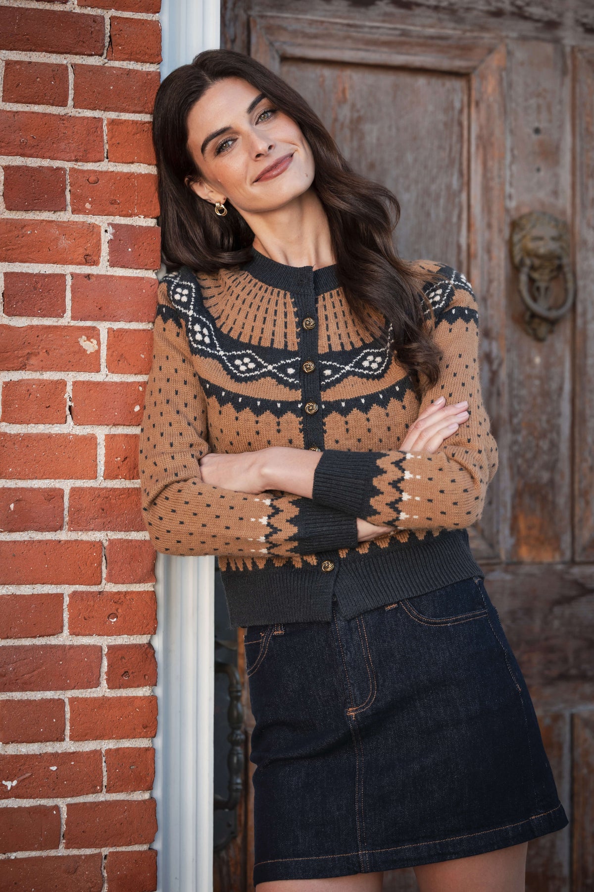 Tan and black patterned cardigan with geometric knit design, button front, and ribbed black trim worn over denim skirt.