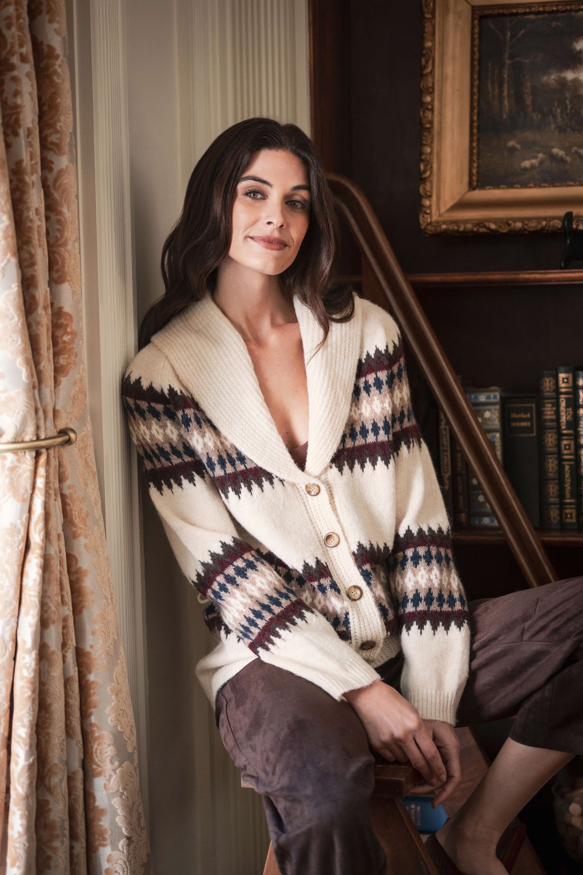Cream cardigan with black, burgundy and navy geometric pattern on sleeves and shoulders, worn buttoned over dark pants.