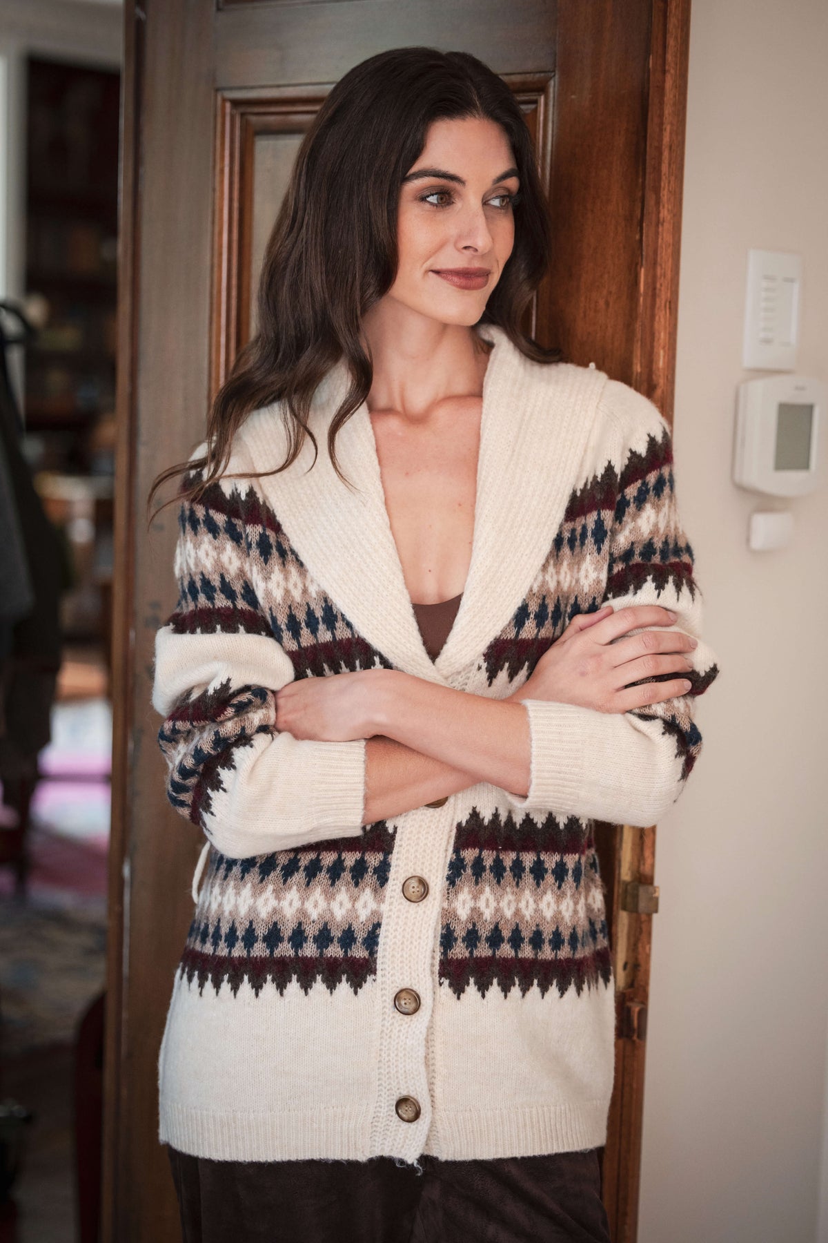 Cream cardigan with navy, burgundy, and tan geometric pattern on sleeves and torso, button front, worn over black pants.