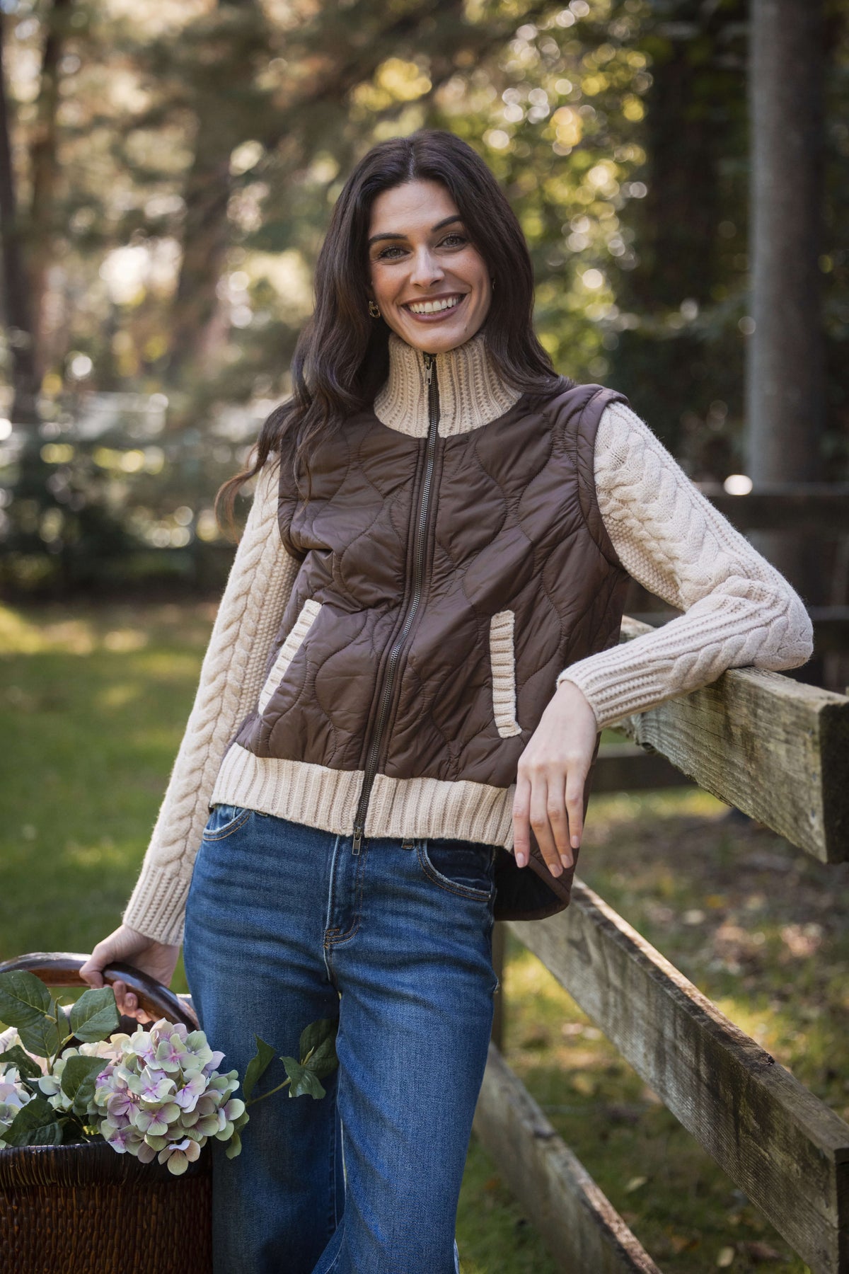 Woman wearing brown quilted vest with cream ribbed knit sleeves, paired with jeans and turtleneck.
