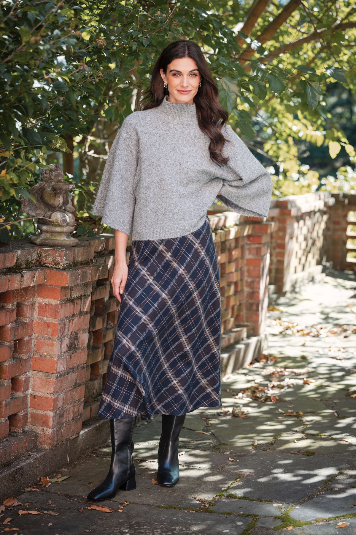 Woman wearing gray turtleneck sweater with three-quarter sleeves and navy plaid midi skirt with black boots.