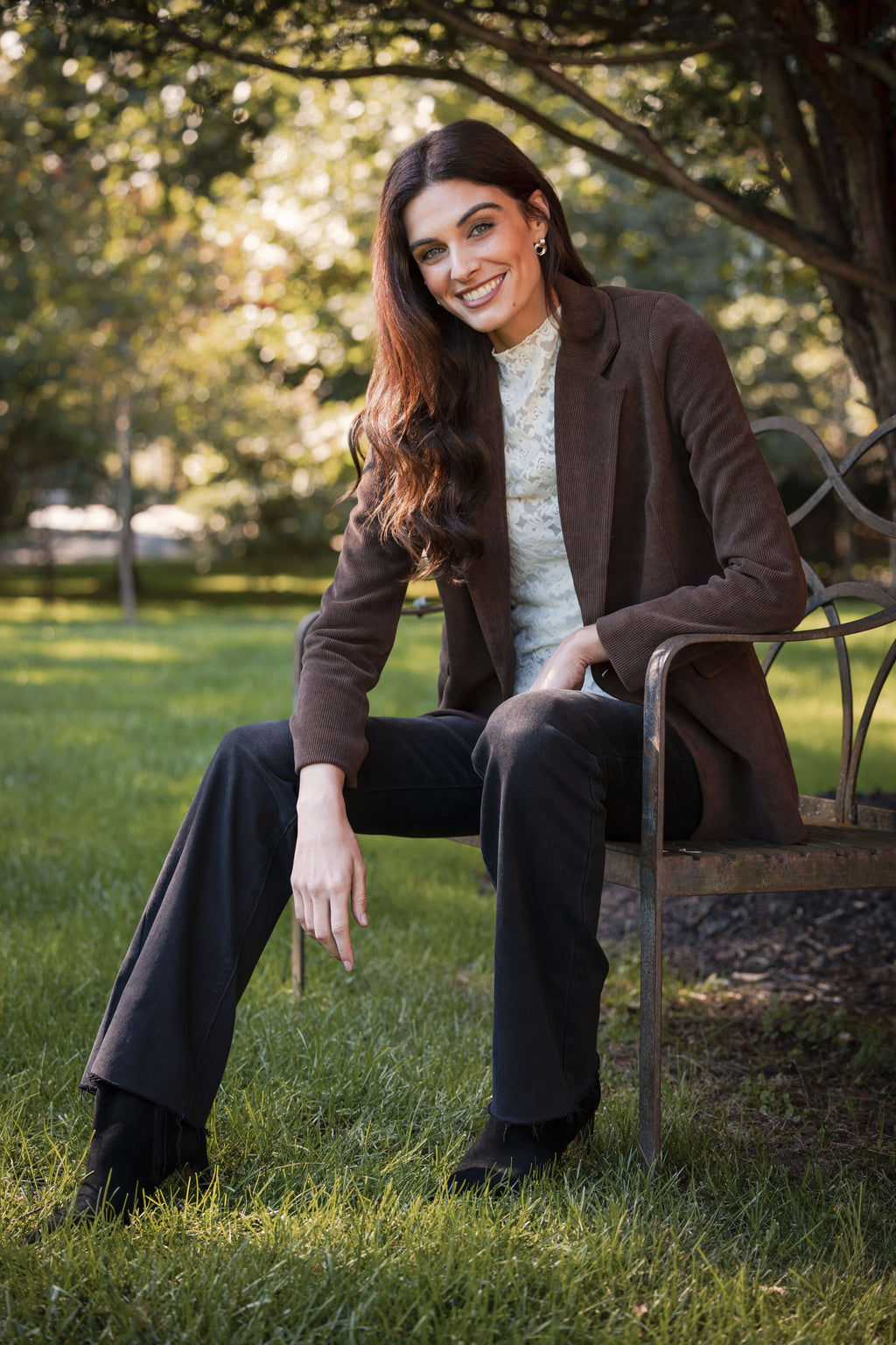 Woman wearing a white lace mockneck top under a brown cardigan with dark pants.