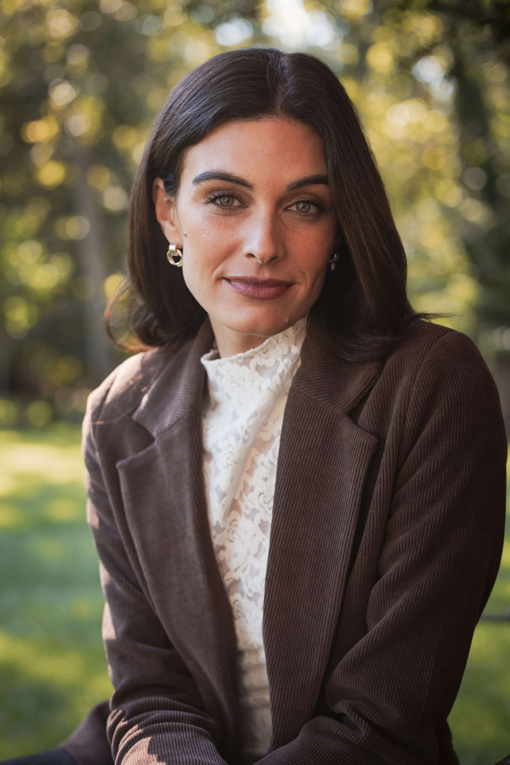 White lace mockneck top with textured pattern worn under a brown cardigan.