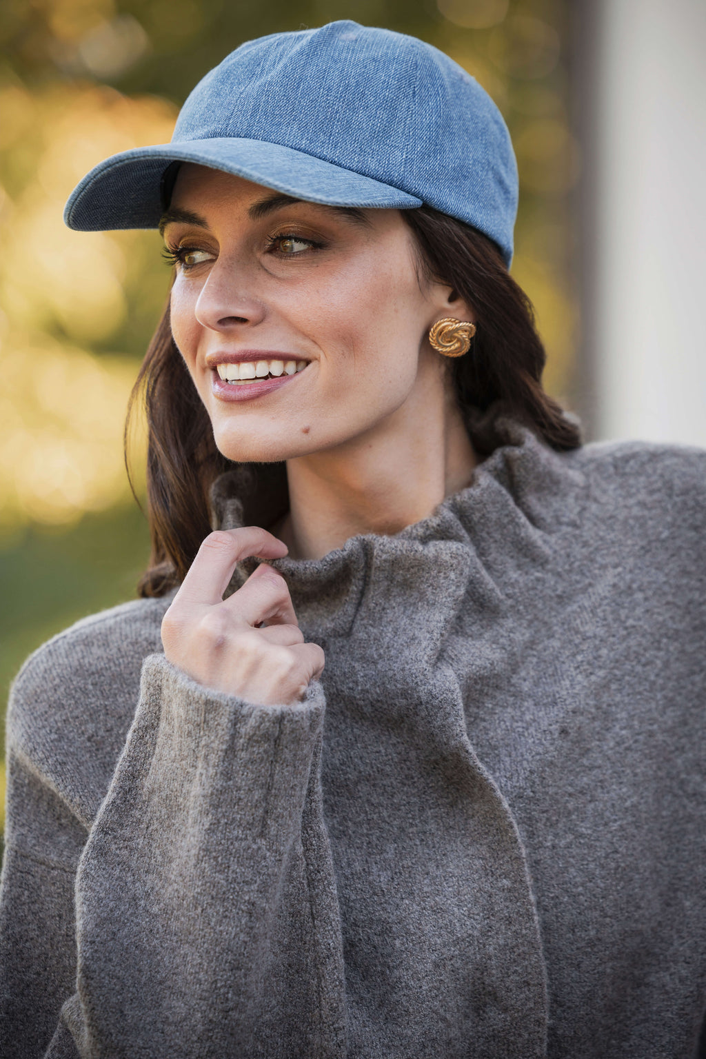 Woman wearing a gray pleated ruffle detail jacket and light blue baseball cap outdoors.