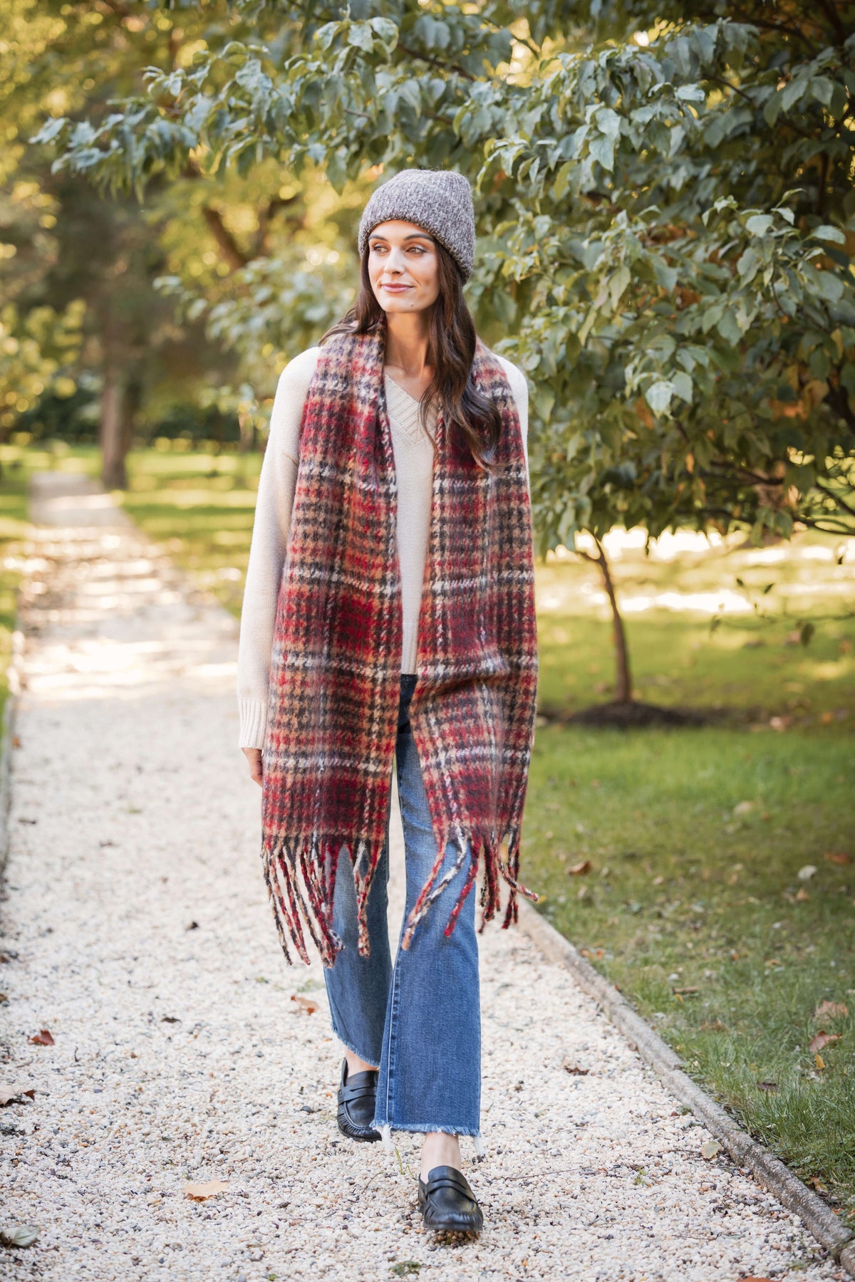 Red and gray houndstooth patterned scarf with fringe trim worn draped over shoulders.