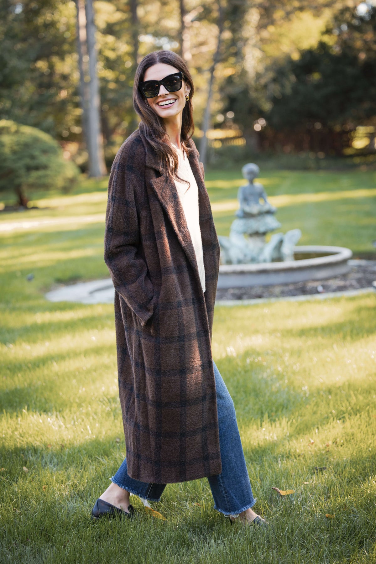 Woman wearing a brown plaid cocoon coat over a white shirt and blue jeans, outdoors.