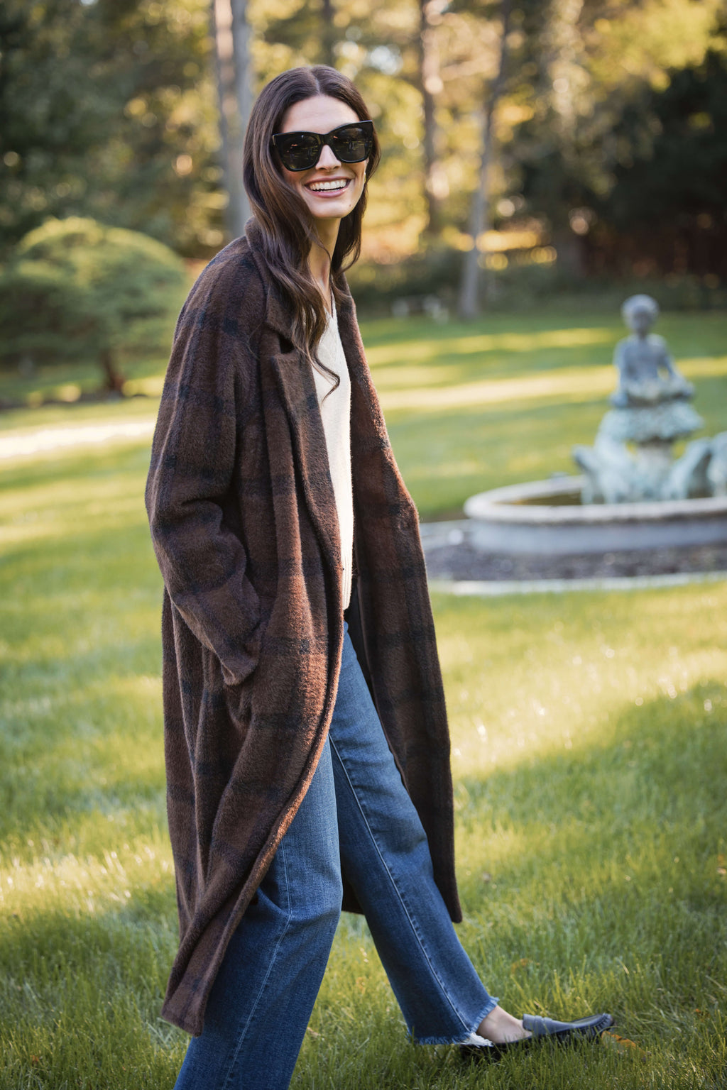 Woman wearing brown open-front cardigan sweater over white v-neck top and blue jeans.