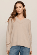 Beige V-neck sweater with ribbed knit texture worn with blue jeans.