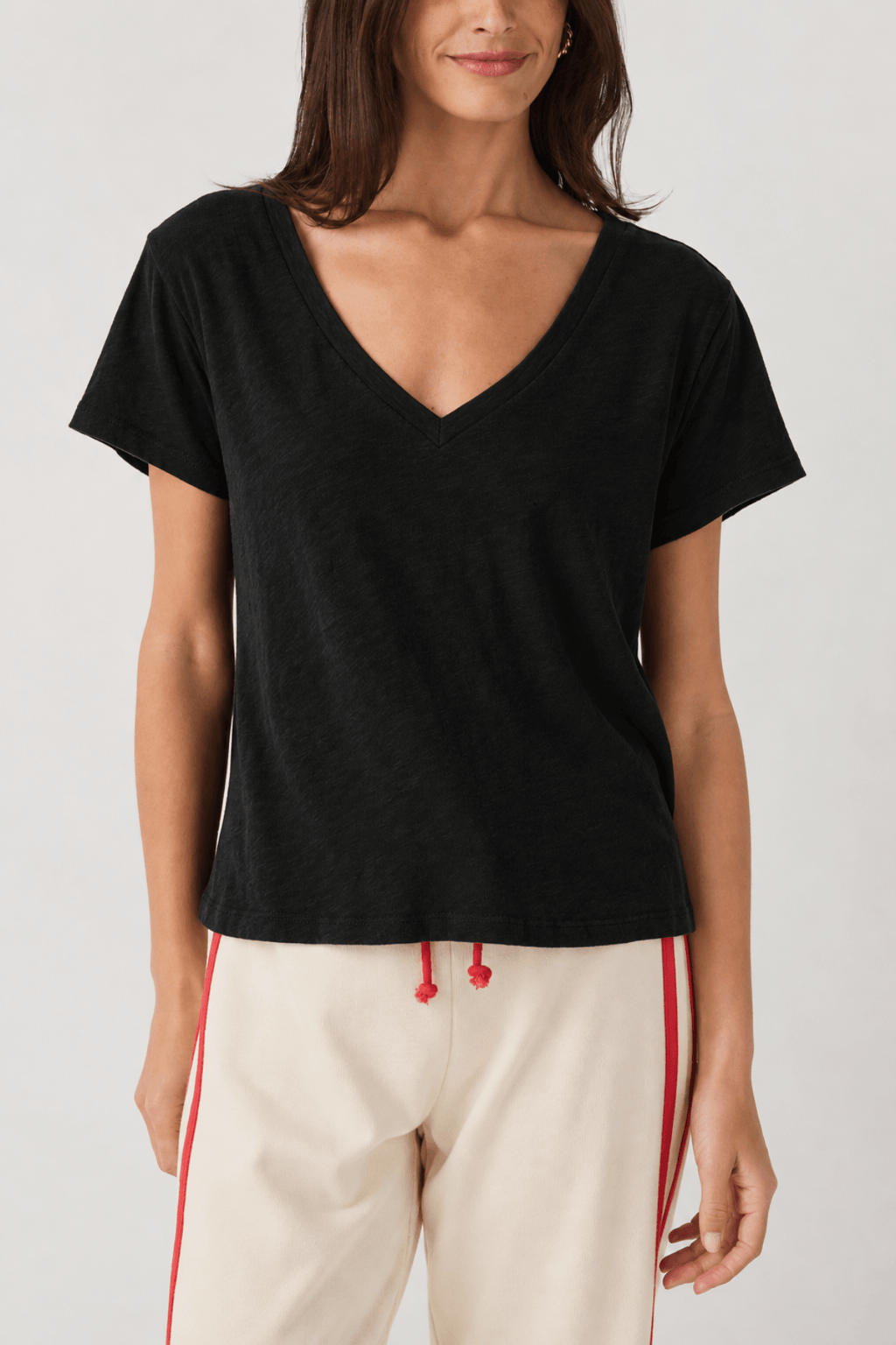 Woman wearing black short-sleeve V-neck tee with cream and red striped pants.
