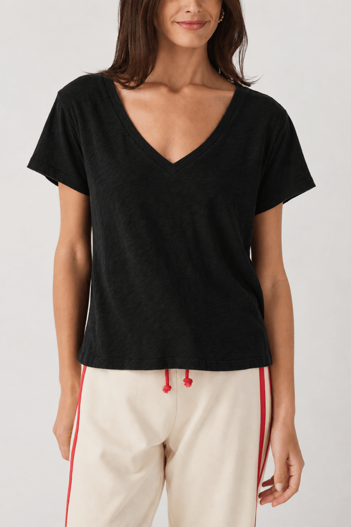 Woman wearing black short-sleeve V-neck tee with cream and red striped pants.