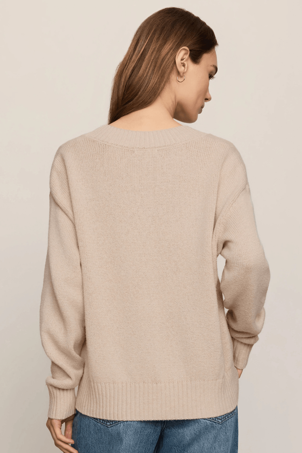 Beige knit V-neck sweater with long sleeves worn with blue jeans, shown from back view.