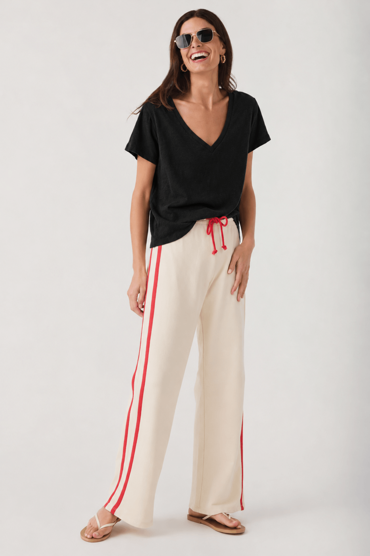 Woman wearing black short-sleeve V-neck tee with cream pants with red side stripes.
