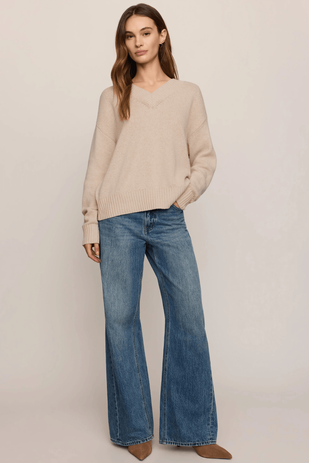 Beige V-neck sweater with ribbed knit texture worn with blue denim jeans.