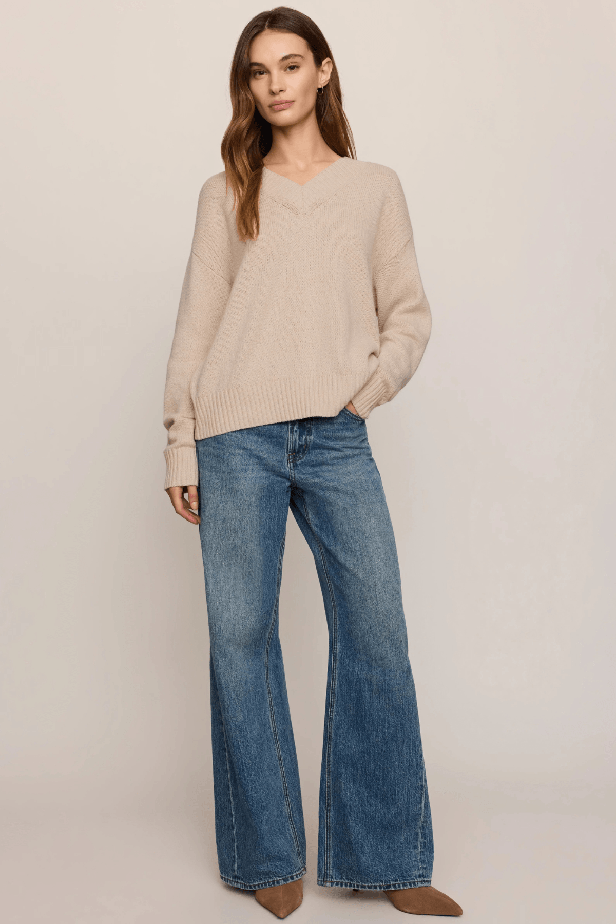 Beige V-neck sweater with ribbed knit texture worn with blue denim jeans.