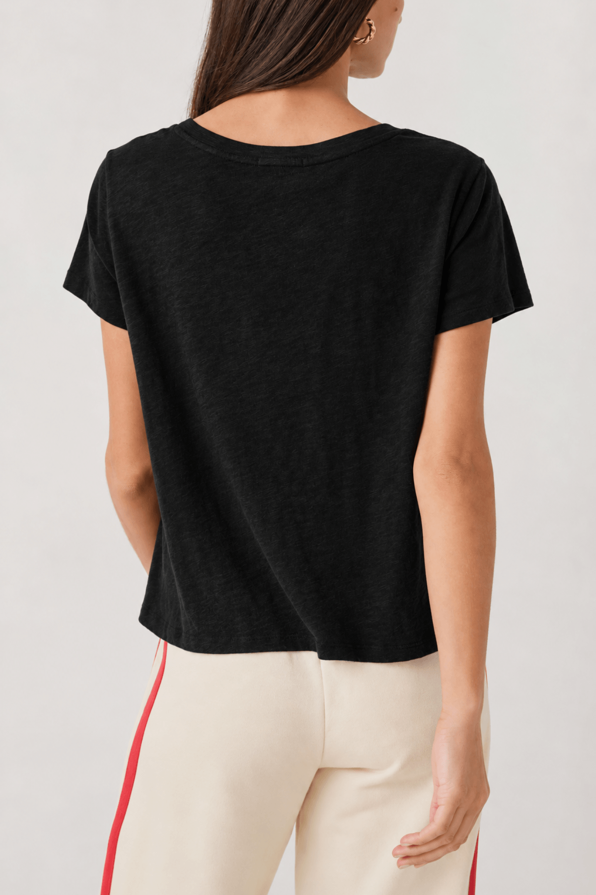 Black V-neck short-sleeve tee worn with cream pants featuring red side stripe.