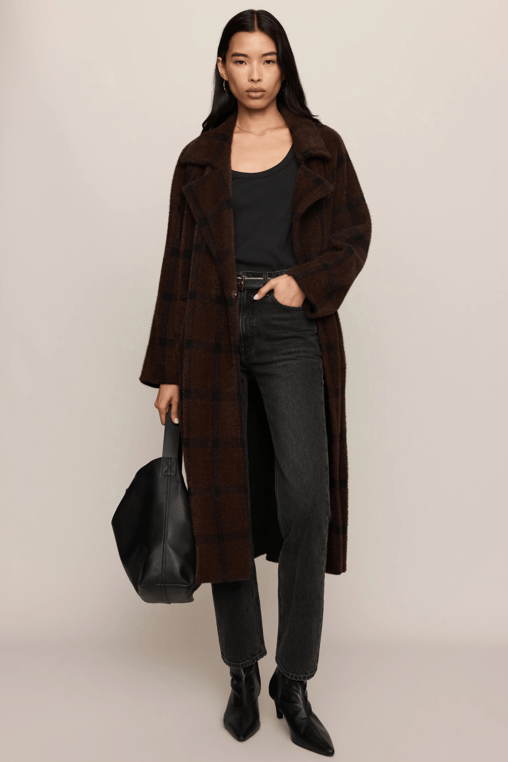 Woman wearing a long brown cocoon coat over a black top and dark jeans with black boots.