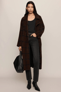 Woman wearing a long brown cocoon coat over a black top and dark jeans with black boots.