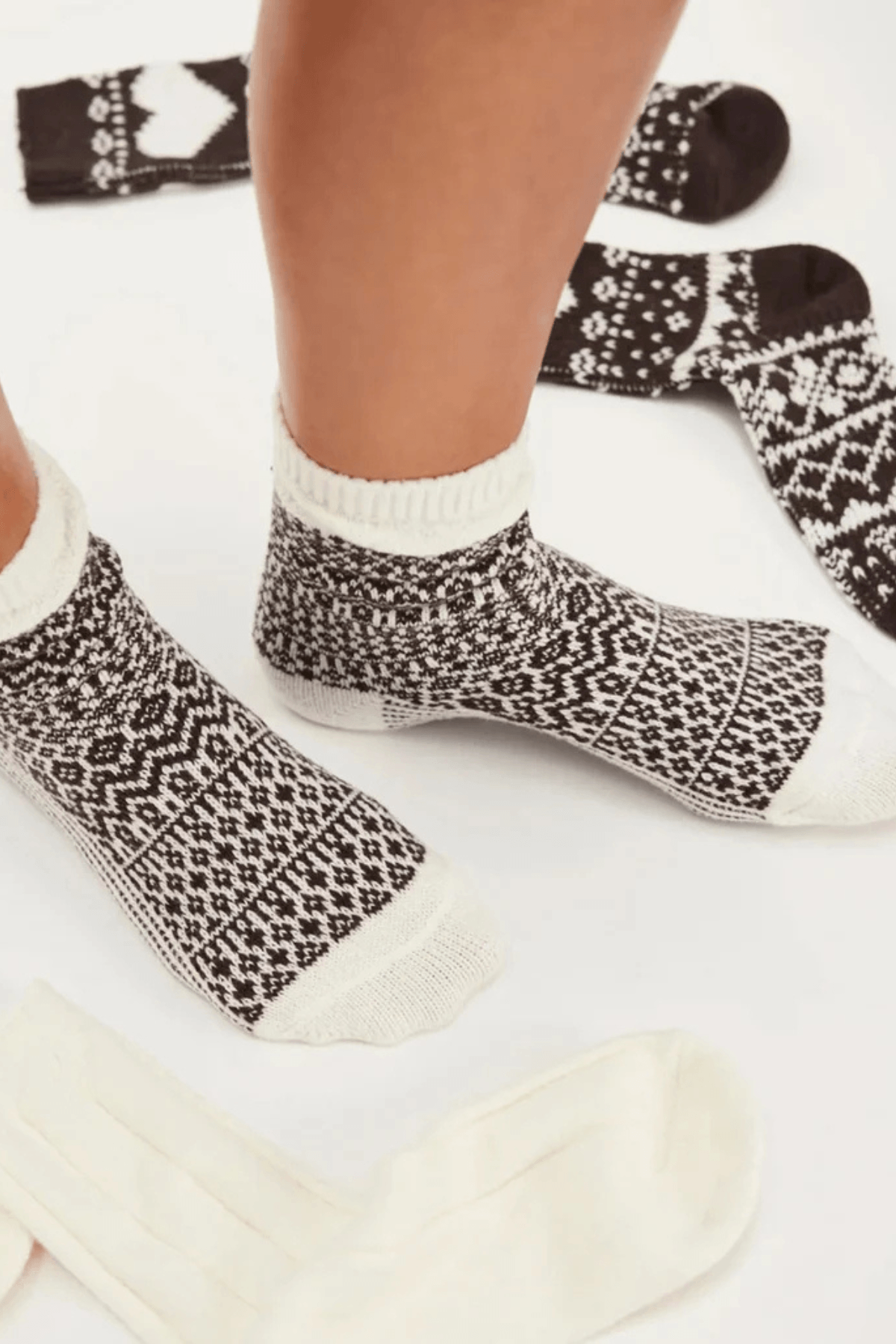 Two feet wear brown and cream patterned knit ankle socks, with more dark Nordic-print socks and plain cream socks laid nearby.