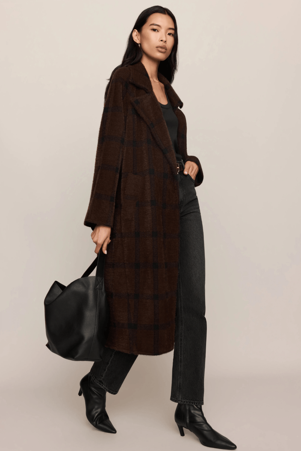 Woman wearing brown plaid cocoon coat over black top and wide-leg pants with black boots and shoulder bag.