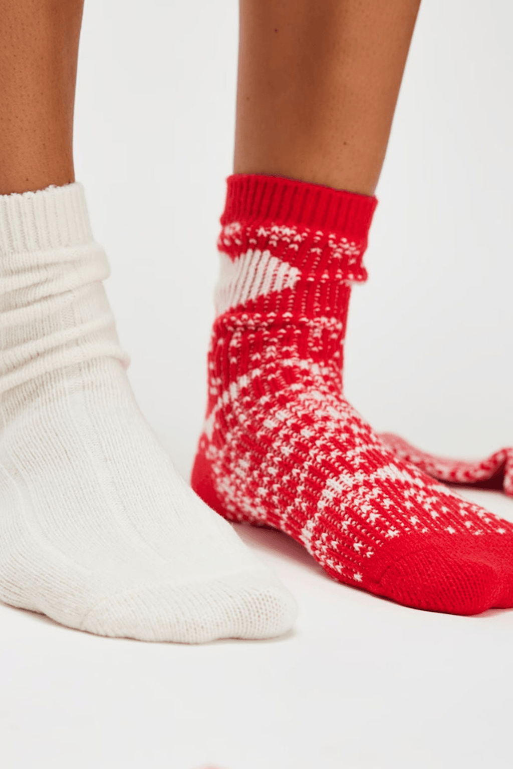 Two feet wear chunky socks, one solid cream ribbed knit and the other red with a white Nordic pattern.