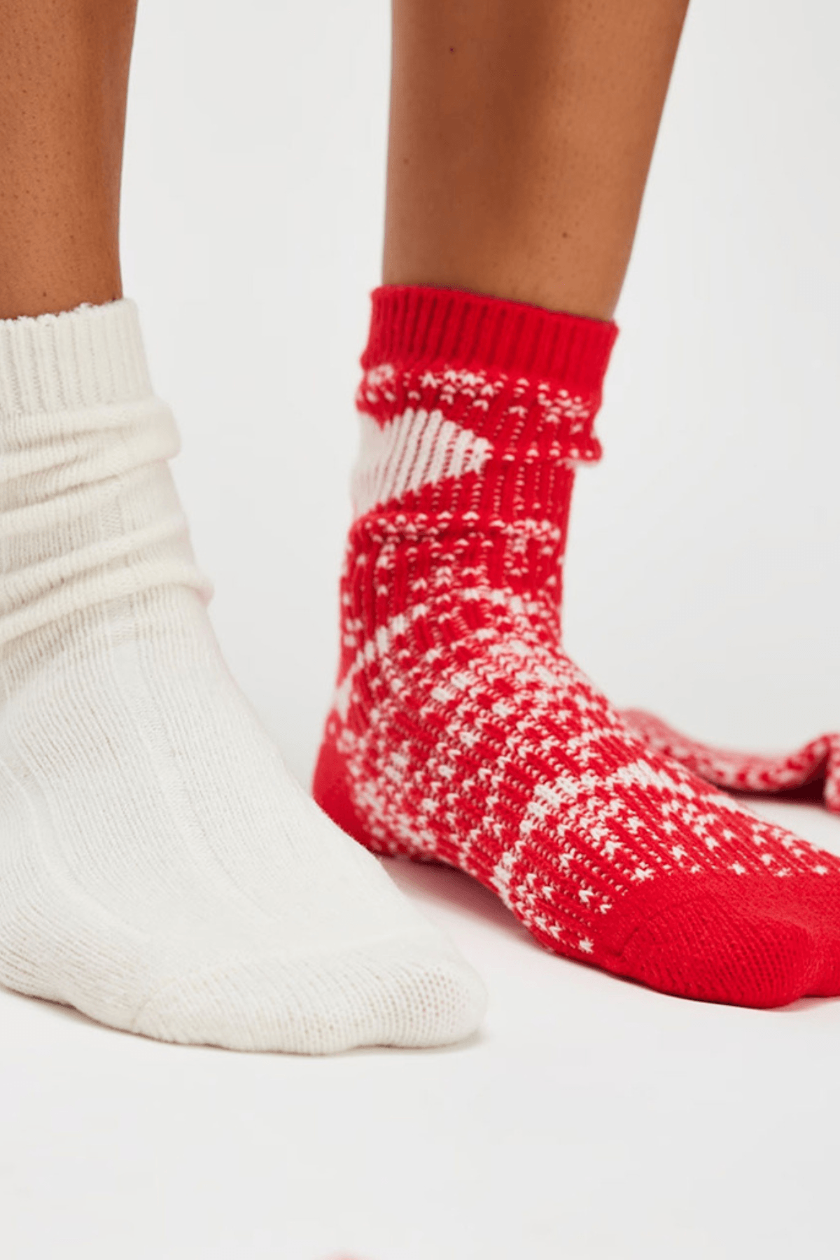 Two feet wear chunky socks, one solid cream ribbed knit and the other red with a white Nordic pattern.