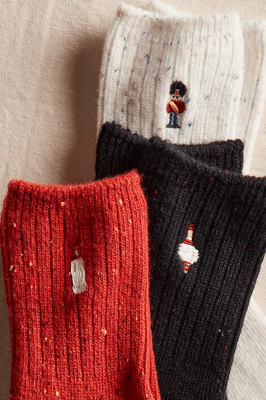 Three ribbed, speckled socks in cream, black, and red feature small embroidered toy soldier, ornament, and drum designs.