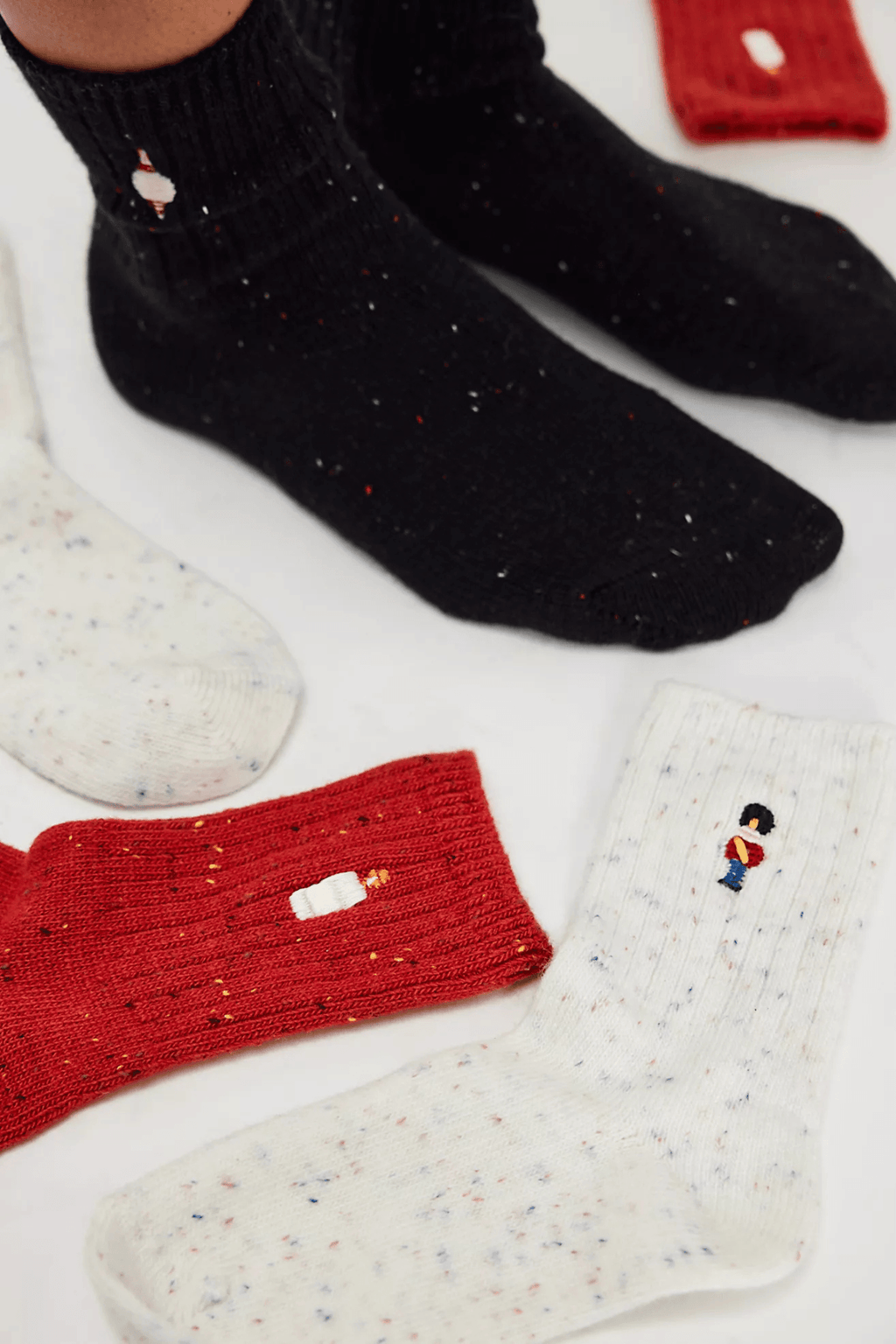 Speckled ribbed socks in black, red, and cream, each embroidered with a small toy soldier, shown worn and laid flat.
