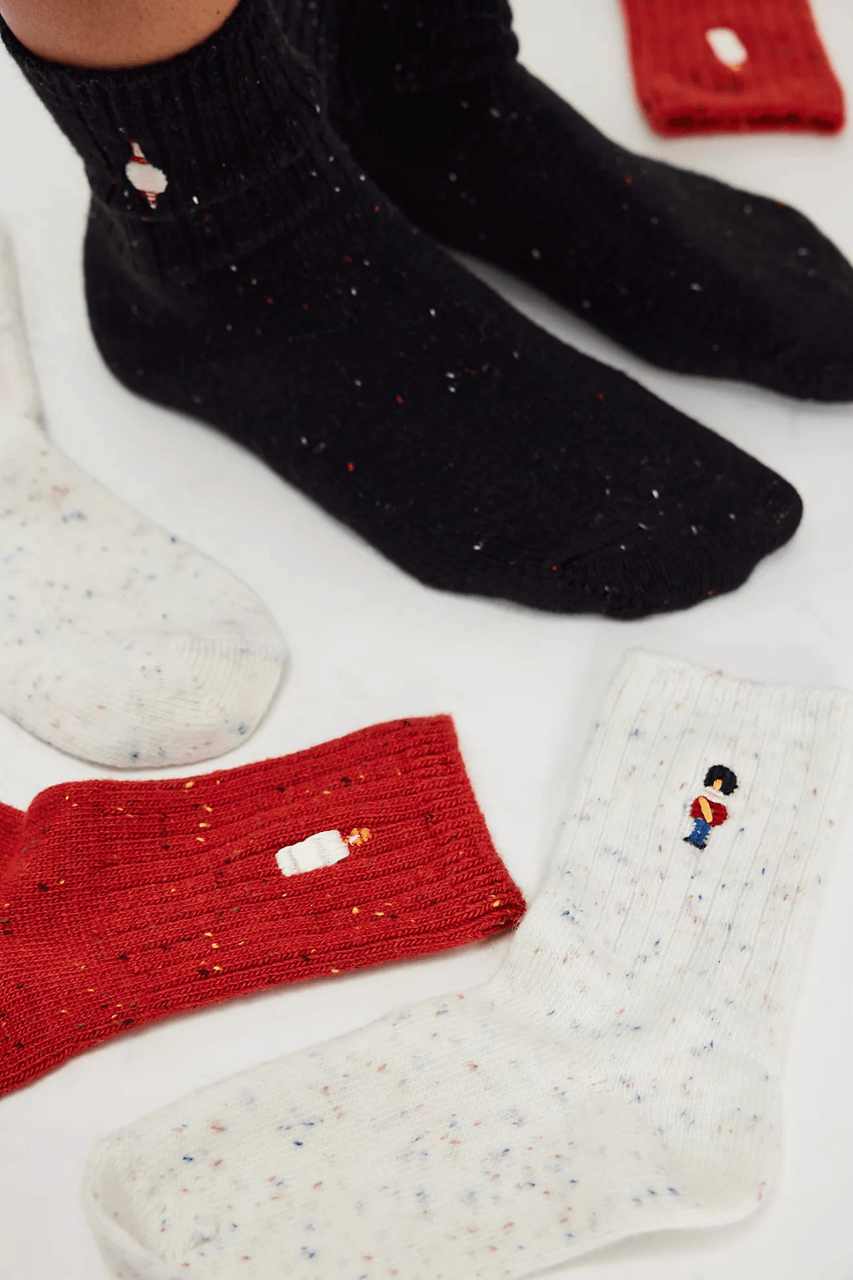 Speckled ribbed socks in black, red, and cream, each embroidered with a small toy soldier, shown worn and laid flat.