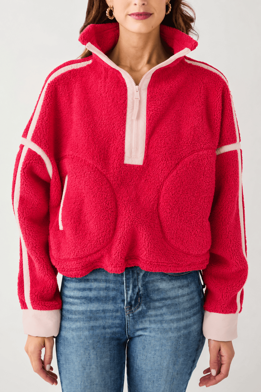 A person wears a red fleece half-zip pullover with pale pink trim and rounded front pockets, paired with blue jeans.