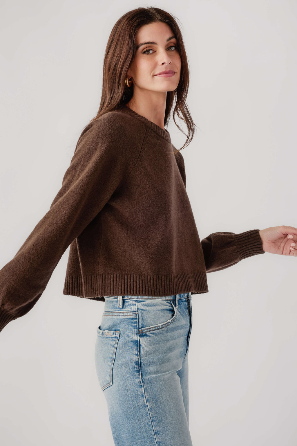 Dark brown crewneck knit sweater with ribbed cuffs and flared hem, side view