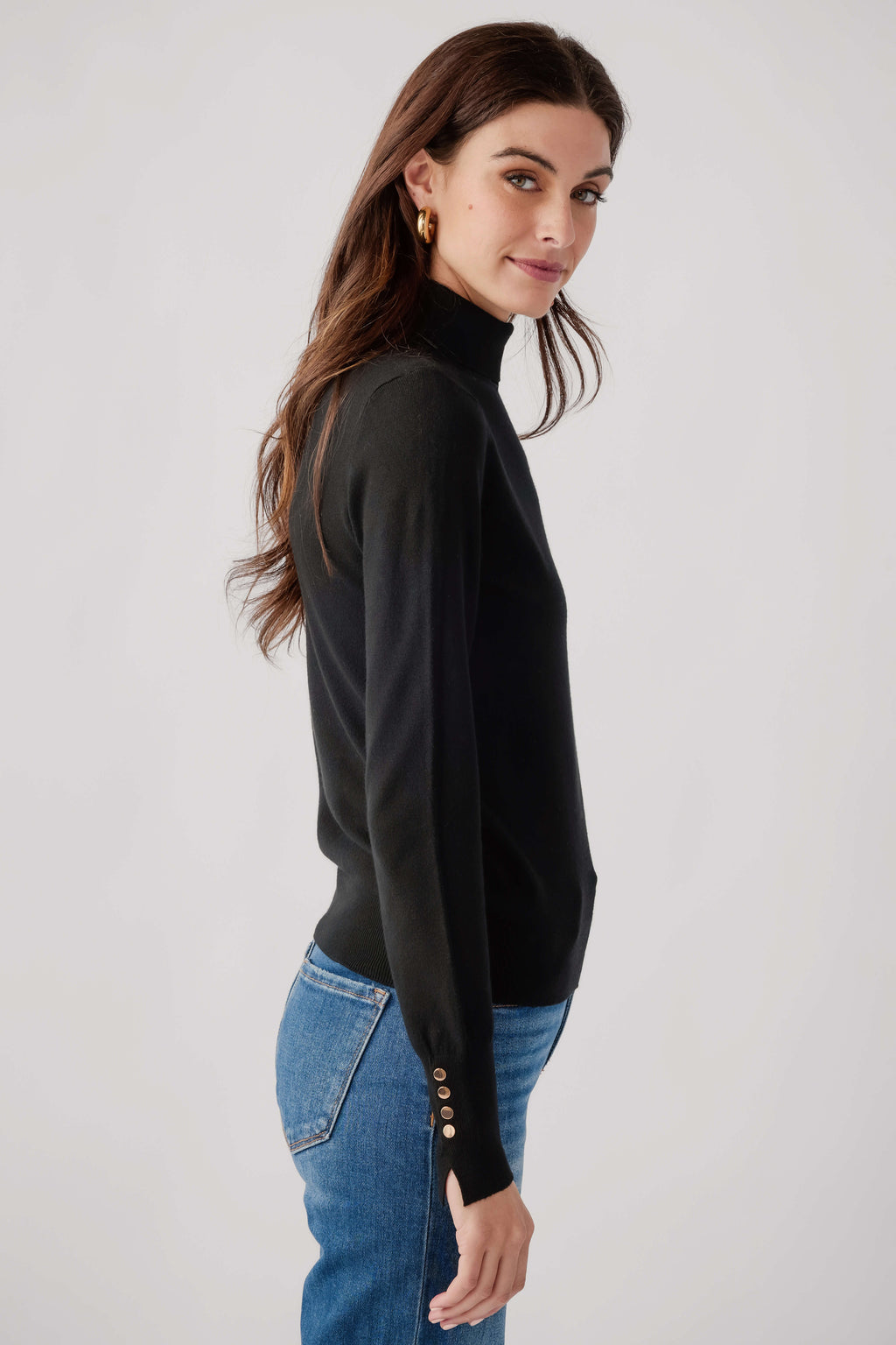Black knit turtleneck top with long sleeves and studded cuffs, side profile.