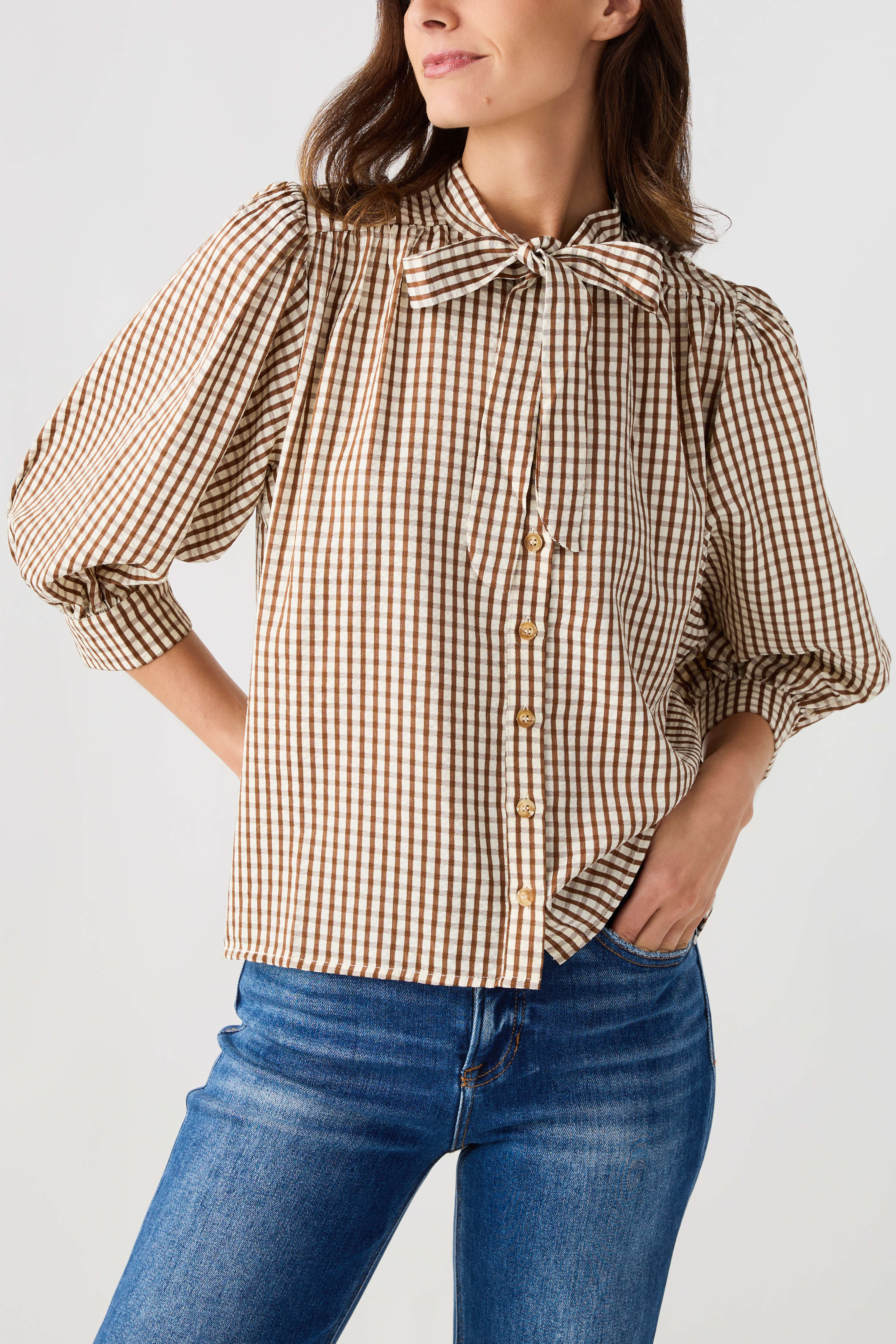 Brown gingham tie-neck blouse featuring a small bow collar and button placket