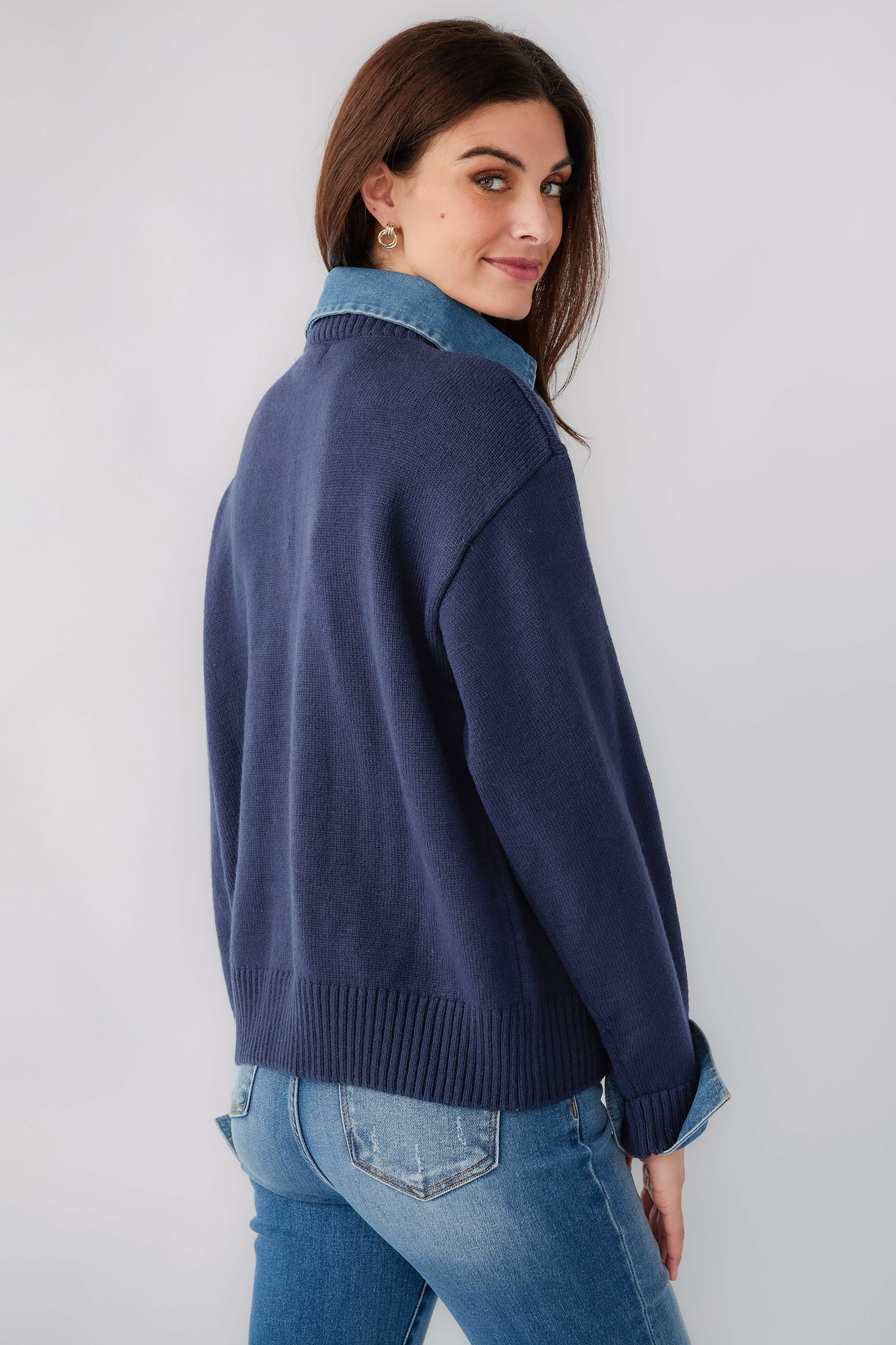 Navy denim polo sweater in side view, chambray cuffs and ribbed bottom hem