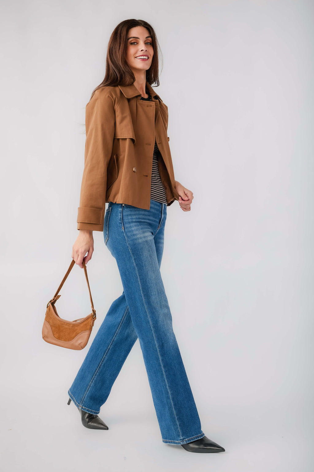 Brown cropped trench jacket worn with blue jeans, side walking view