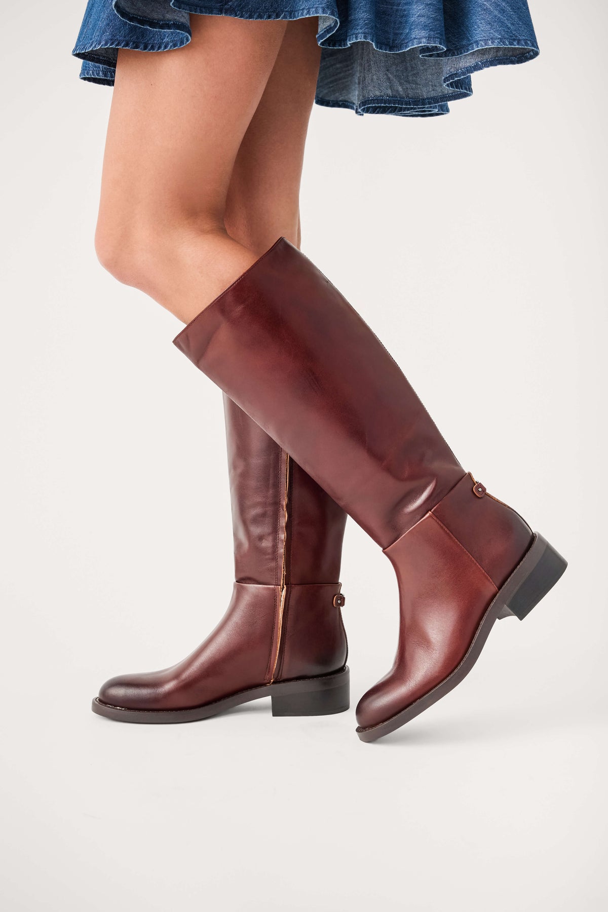 Dark brown leather knee-high boots angled side view, low stacked heel and buckle detail