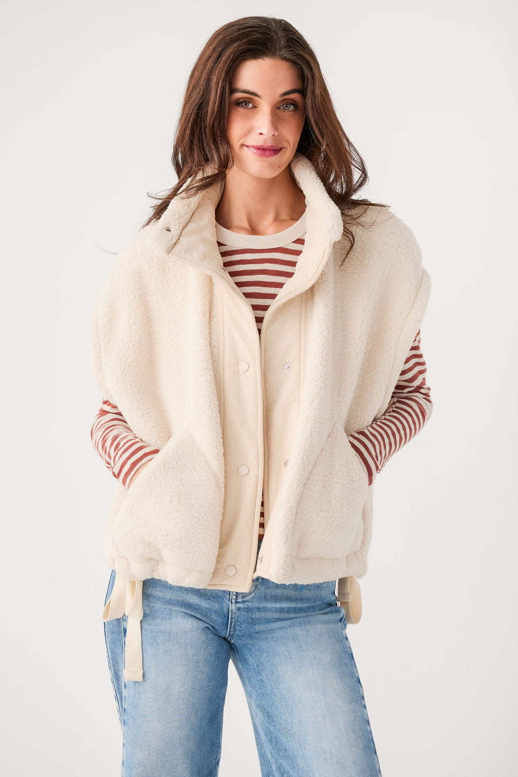 Cream fleece vest with snap buttons and high collar, model wearing it open over striped shirt.