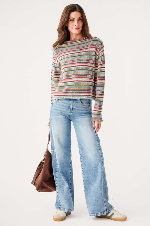 Woman wearing a multicolored striped rollneck sweater with light blue jeans and cream sneakers.