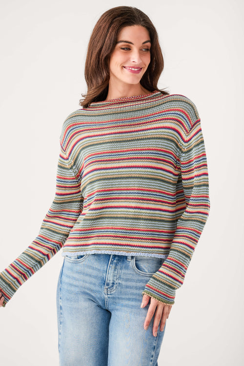 Multicolor striped rollneck sweater with horizontal bands of red, blue, yellow, and gray on a woman wearing light blue jeans.