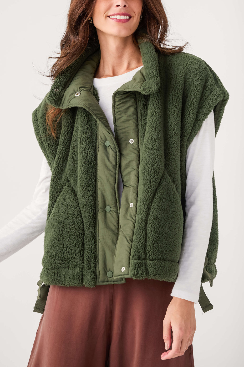 Dark green fleece vest with snap buttons and stand collar, model wearing it over a white shirt.