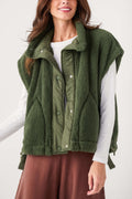 Dark green fleece vest with snap buttons and stand collar, model wearing it over a white shirt.
