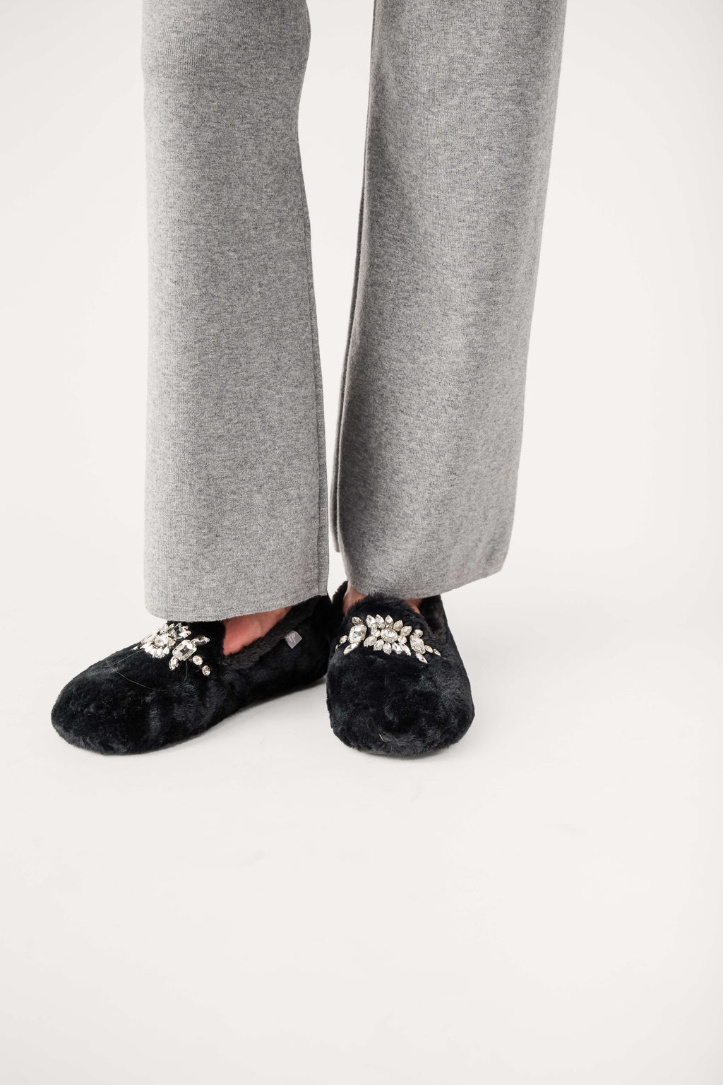 Black fuzzy loafer slippers with jeweled floral embellishment at instep