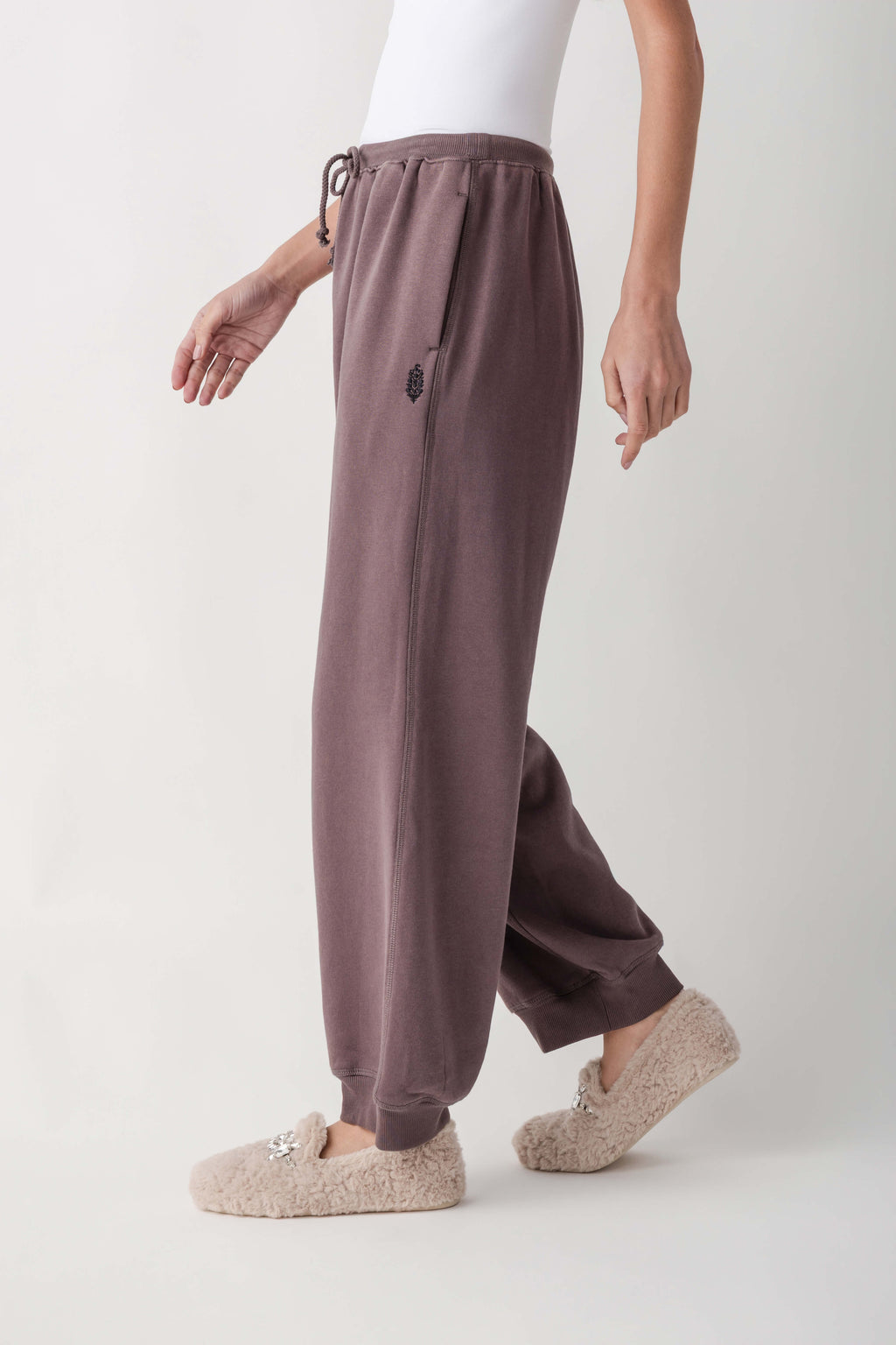 Mauve joggers with drawstring waist, small logo detail, and tapered ankles worn with cream fuzzy slippers.