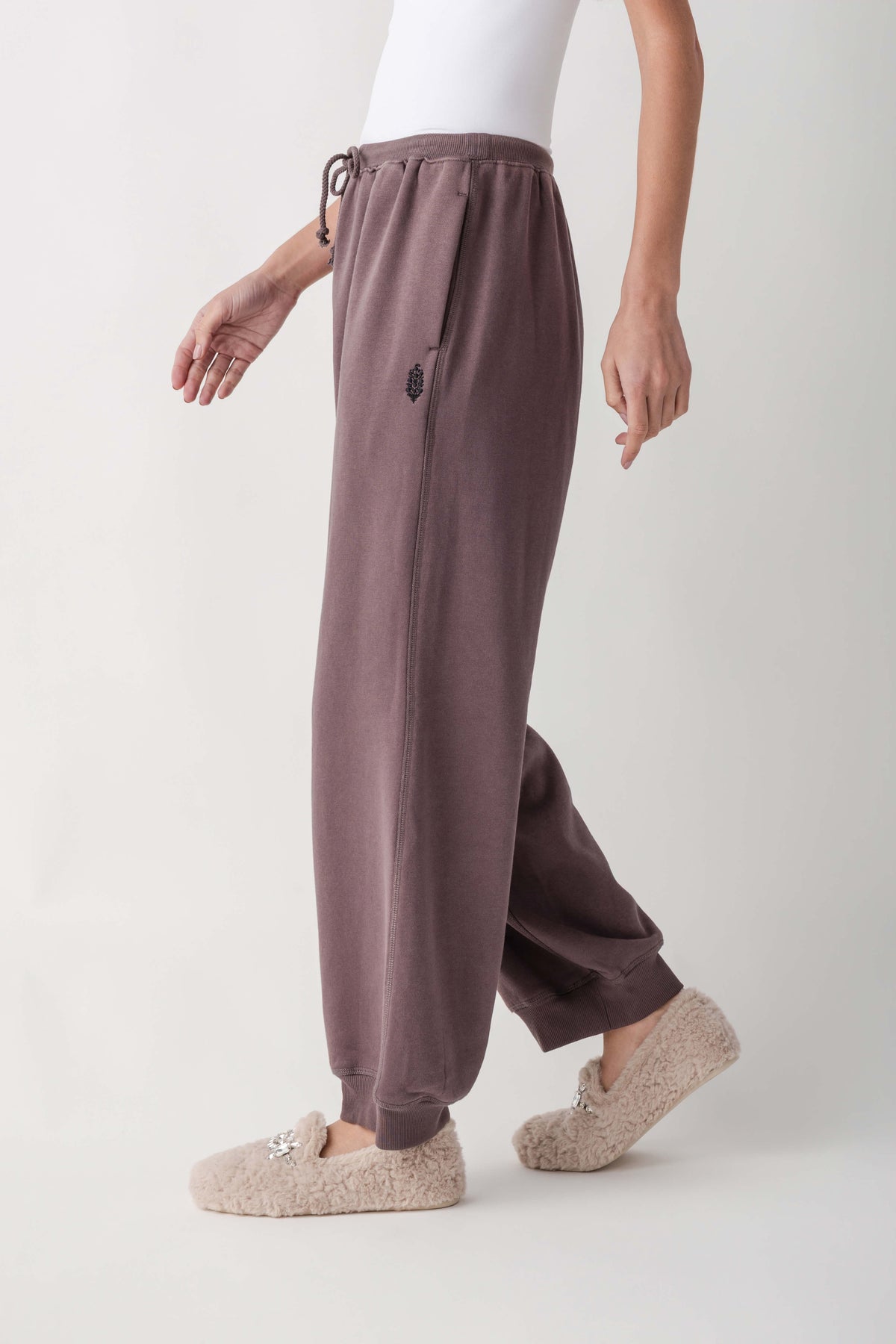 Mauve joggers with drawstring waist, small logo detail, and tapered ankles worn with cream fuzzy slippers.