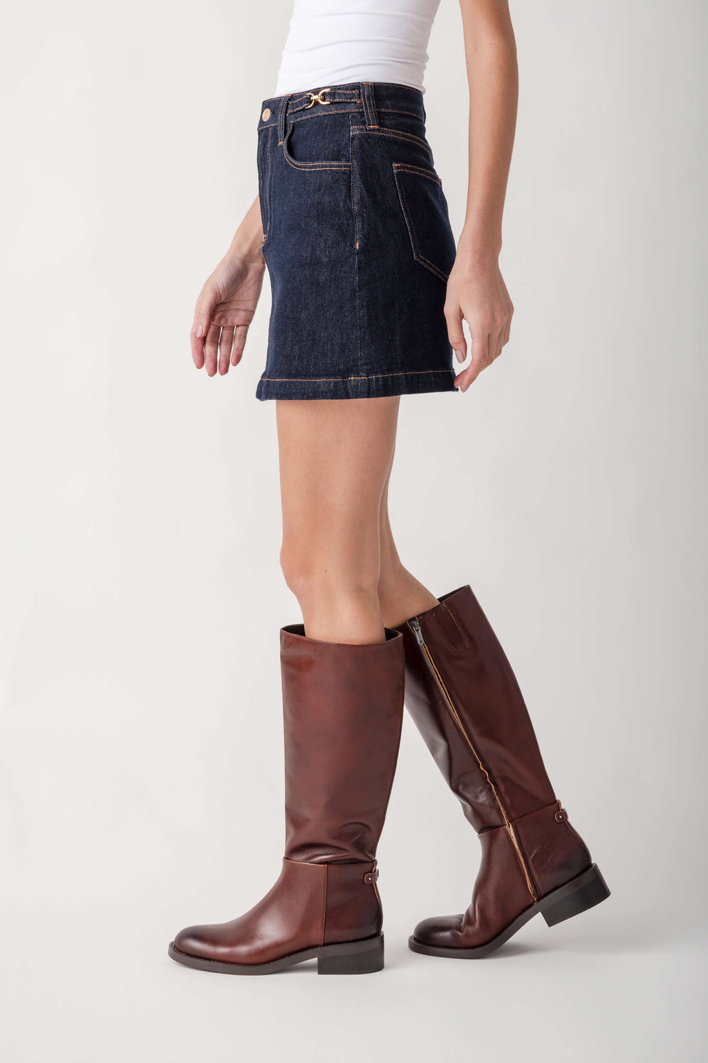 Dark wash denim mini skirt with gold belt detail and front pockets paired with burgundy knee-high boots.