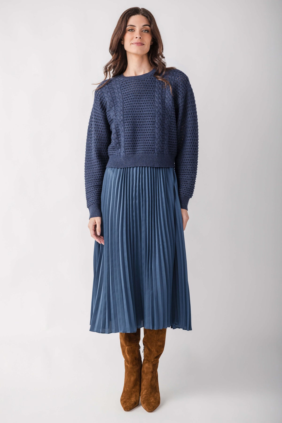 Woman wearing blue textured knit sweater top with pleated skirt bottom and brown suede boots.