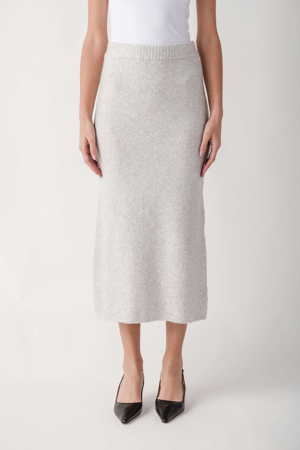 Cream ribbed knit midi skirt with elastic waistband worn with white tank top and black pointed heels.