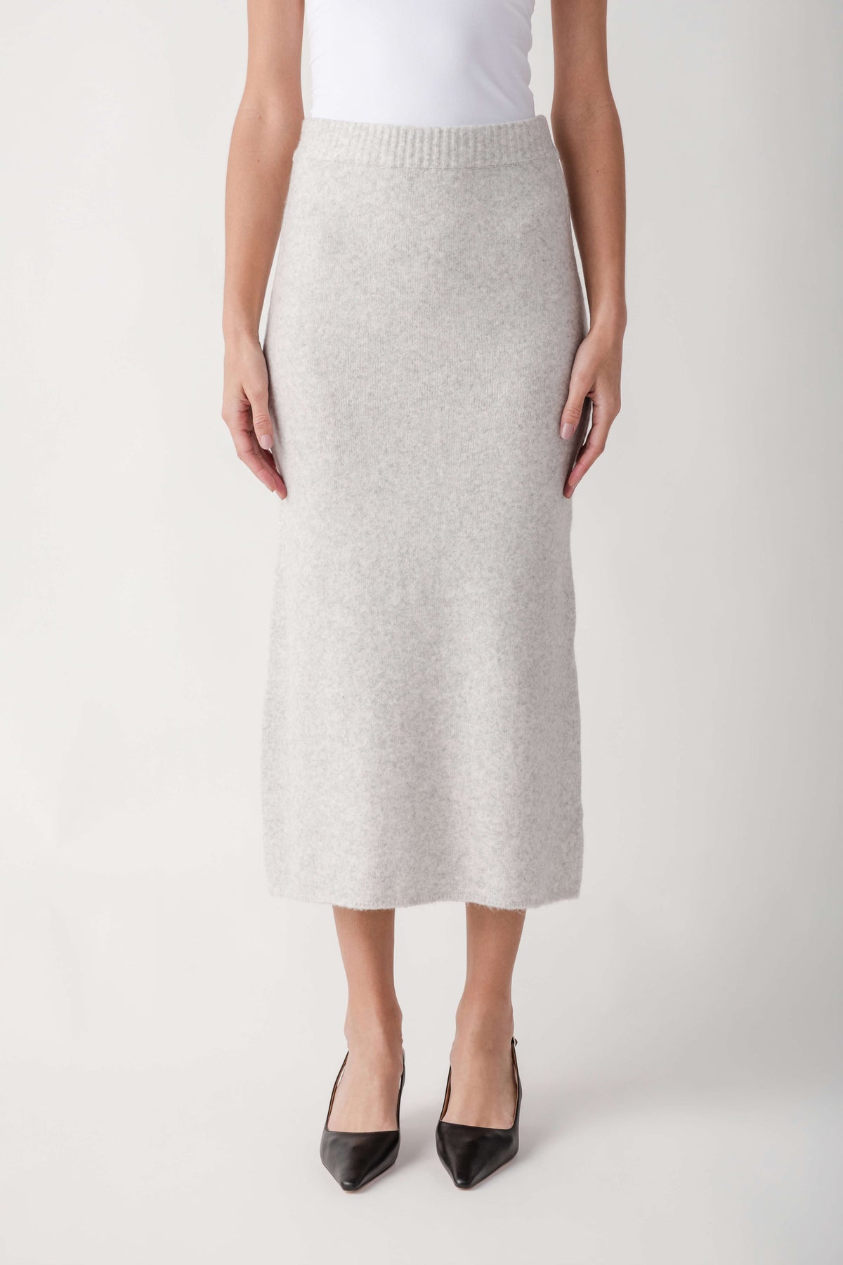 Cream ribbed knit midi skirt with elastic waistband worn with white tank top and black pointed heels.